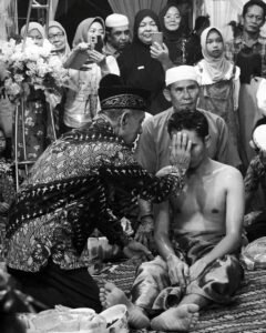 Seorang sesepuh membaluri pupur pada mempelai pria